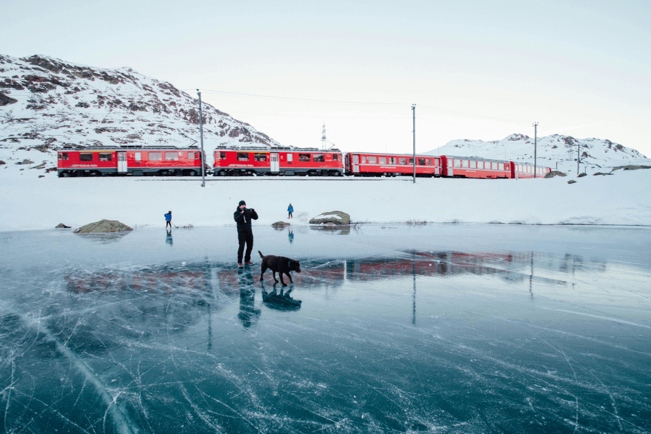 스위스 열차와 설경: a person standing on a frozen lake with a dog